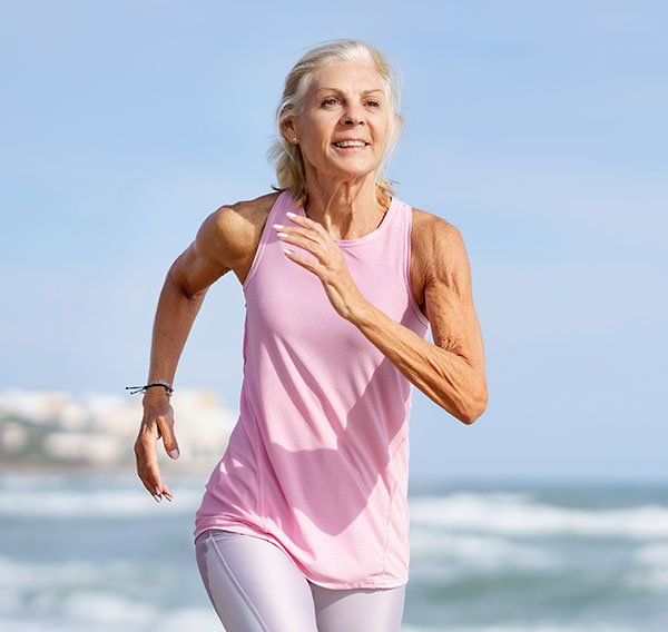 Ältere Frau joggt glücklich morgens am Strand