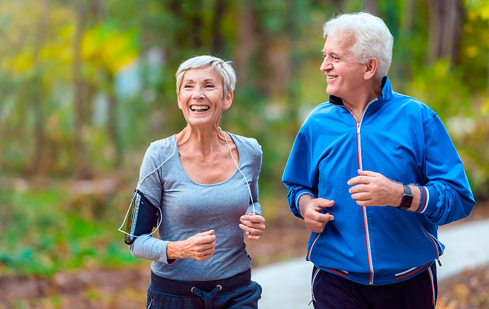 Best Ager Paar joggt durch den Wald und schauen glücklich