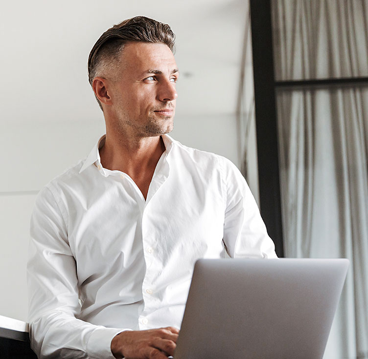 Entschlossener Mann am Laptop schaut souverän Richtung Fenster