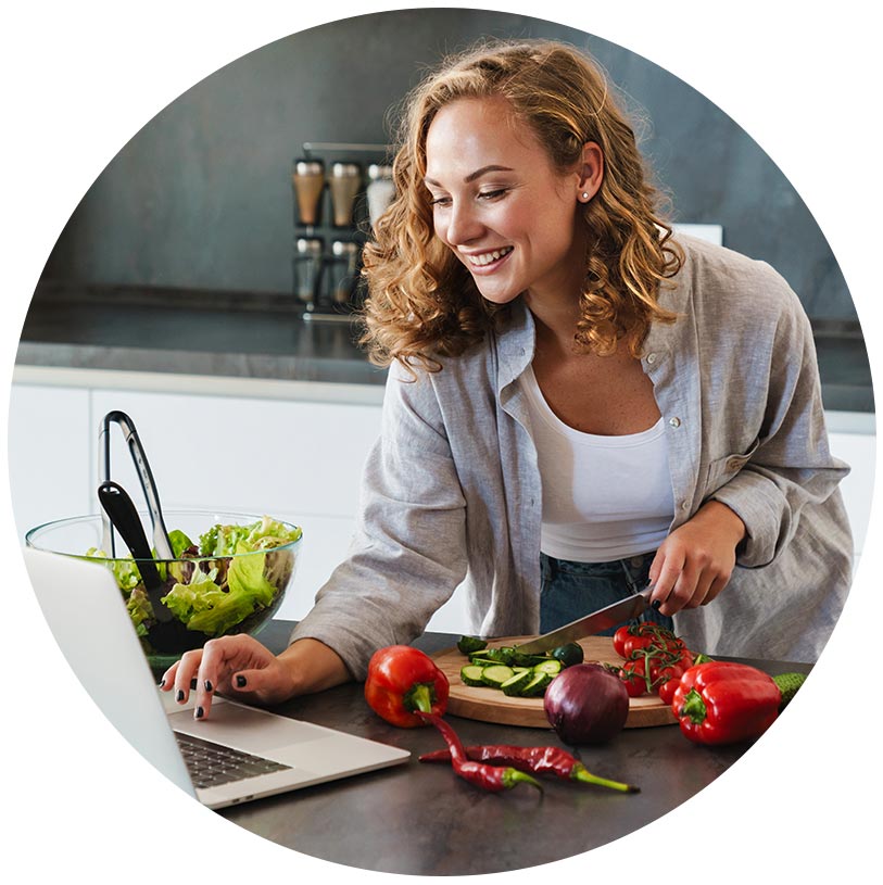 Junge Frau macht Salat nach Rezept aus dem Laptop