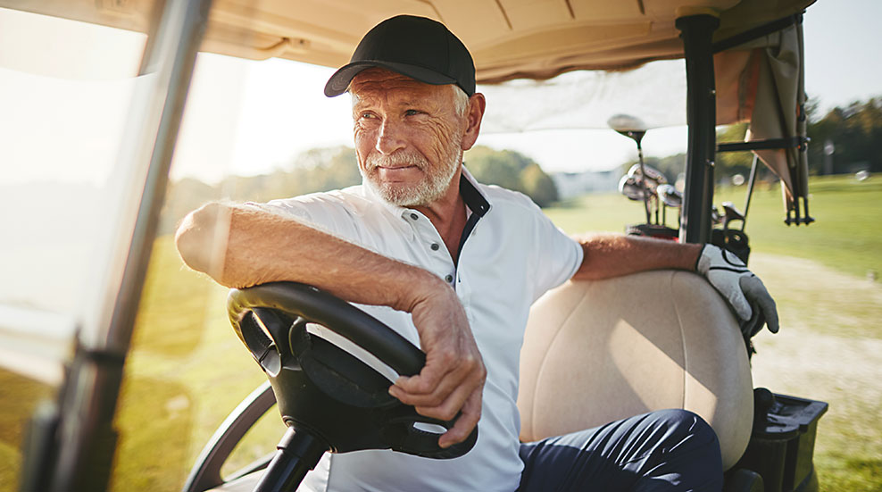 Mann sitzt zufrieden im Golfwagen und schaut nach vorne