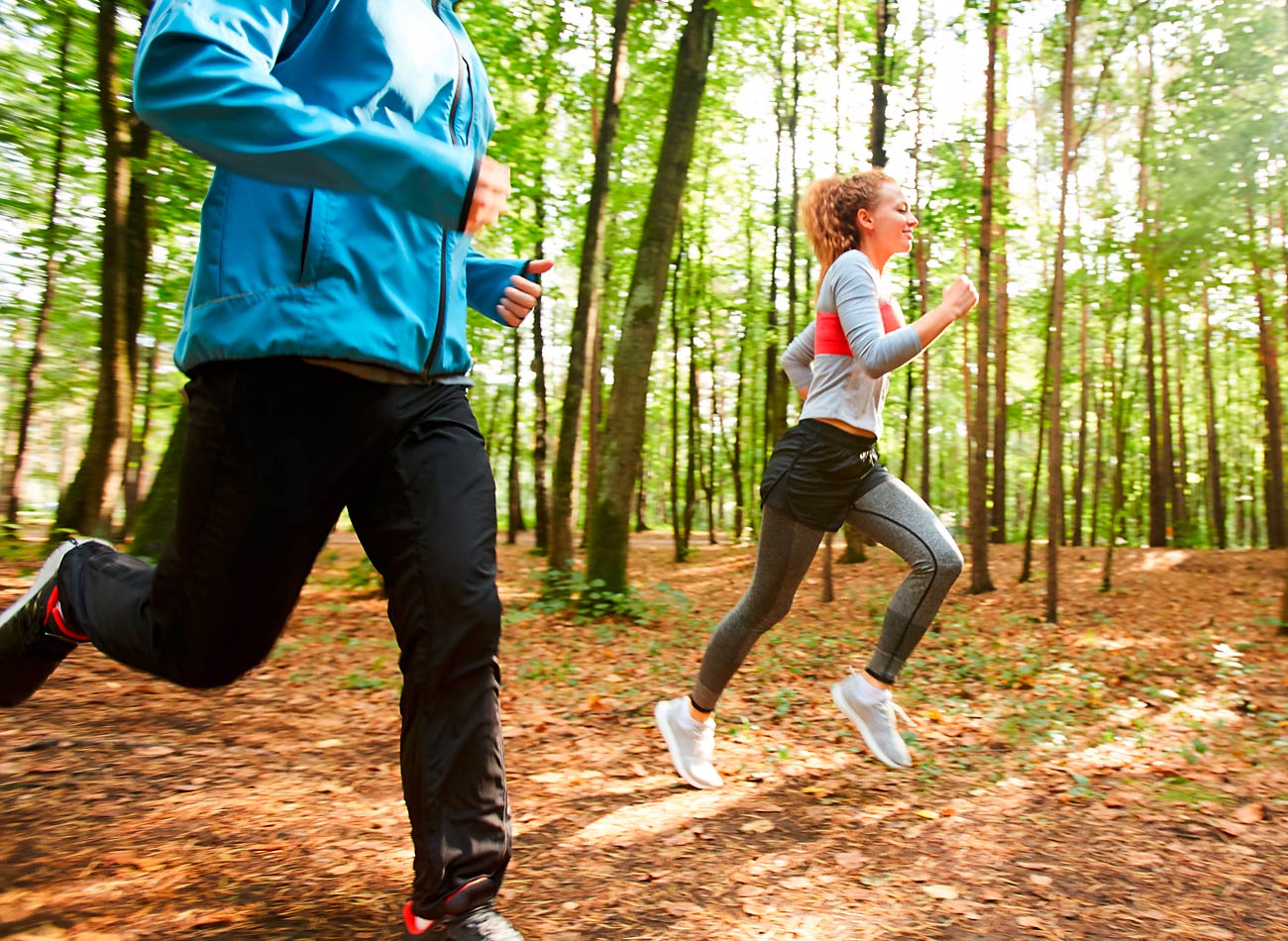 Personal Trainer joggt mit junger Frau durch den Wald