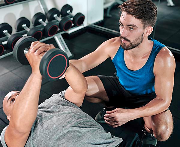 Personal Trainer korrigiert seinen Kunden im Fitness Studio