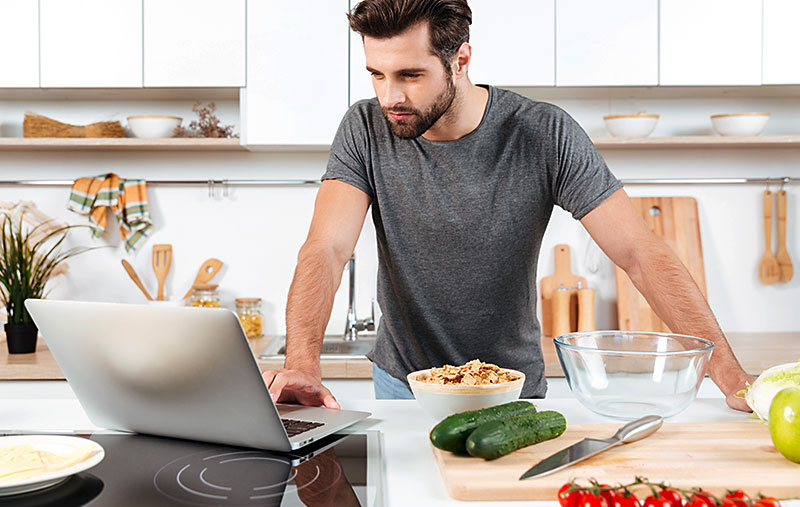 Schlanker Mann kontrolliert seine Kalorien am Laptop und kocht nach Rezept