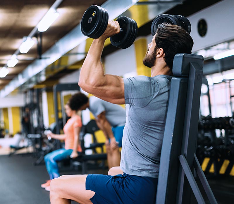 Mann beim Schulterpressen mit Kurhanteln im Gym