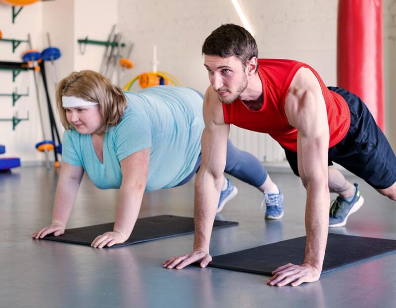 Stark übergewichtige Frau trainiert mit Personal Trainer im Studio