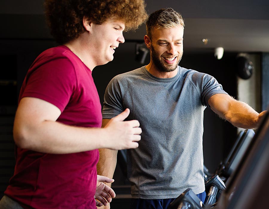 Übergewichtiger Mann trainiert mit Personal Trainer auf dem Laufband